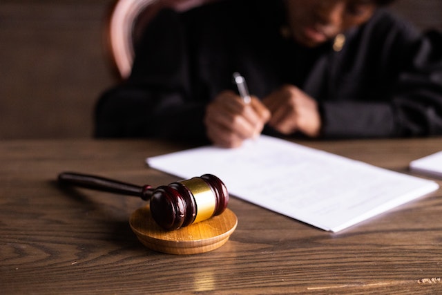 a judge reviews a document at their desk upon which sits a wooden gavel